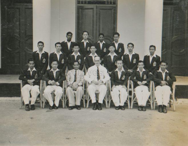 Group photograph of Principal of Raffles Institution E H Wilson (centre) with school prefects: (front row, seated from left to right) Ratty, Lee Hoe Guan, Mr K M R Menon, Wong Poh Wah, Khoo Boo Yee, Abdul Jamil; (second row, left to right) Leong Kok Wing, Boon Kok Peow, Wong Ah Mook, Tan Djin Hock, Chan Swee Chin, Low Ah Yui, Chia Wee Ling; and (back row, left to right) Karmakar, Ng Kim Beng, N Suppiah, Chin Yuen Fook