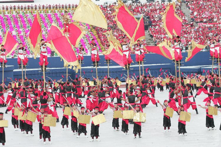 National Day Parade 2006 at National Stadium -- Close-up of mass martial arts display 'Youth Explosion', with soldiers from the 7th Singapore Infantry Brigade being hoisted up on logs waving flags to form 41 "candles" within frame of "birthday cake" formed by students from Rulang Primary School. This pre-parade item is choreographed by MediaCorp artiste Vincent Ng (holding golden flag at top left).
