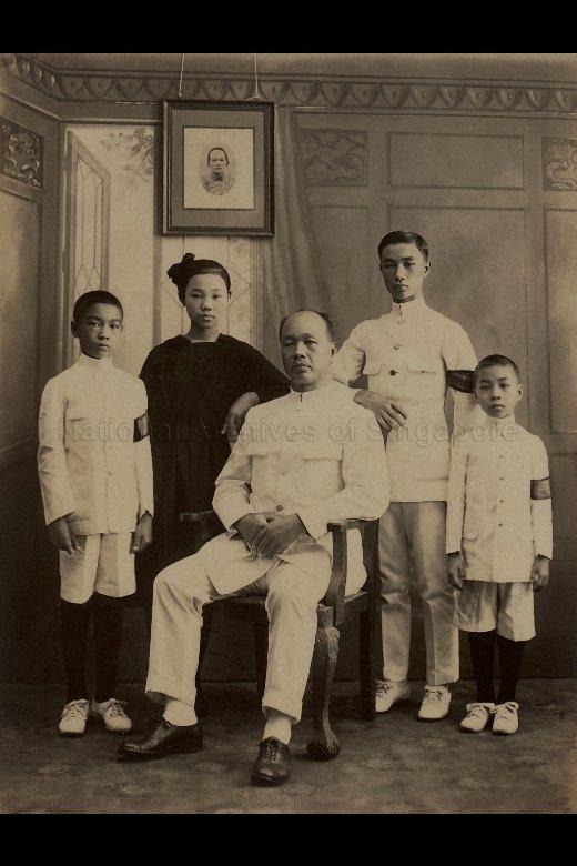 The seated man is Koh Peng Chiang (許炳昌). The woman who died was his first wife, Maria Ng Sok Eng (黃淑英). His children stand around him from left to right: Koh Guan Yam (許元炎), Dorothy (Dora) Koh Lao Hueh (許老花; married name Ts'ai), Koh Koon Yam (許坤炎), Joseph Koh Cheng Yam (許清炎). Koh Cheng Yam was father of Diana Koh, who donated this photograph. This studio photograph was probably taken shortly after Madam Ng's death in 1919.