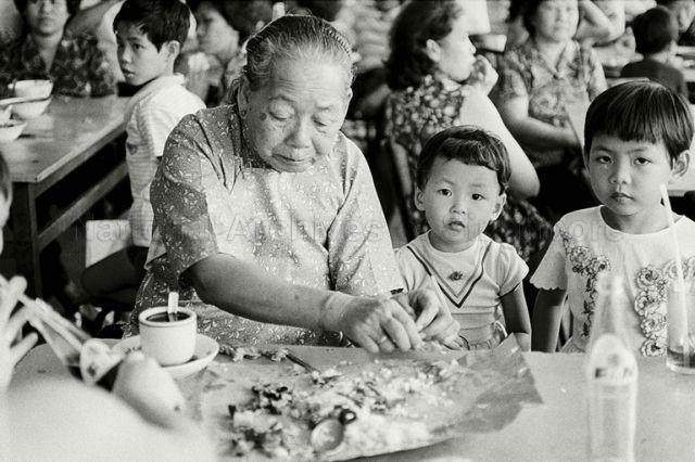 Exhumation of Chinese graves at Kampong San Teng cemetery in the 1980s: A grandmother taking care of her grandkids during the salvation rituals