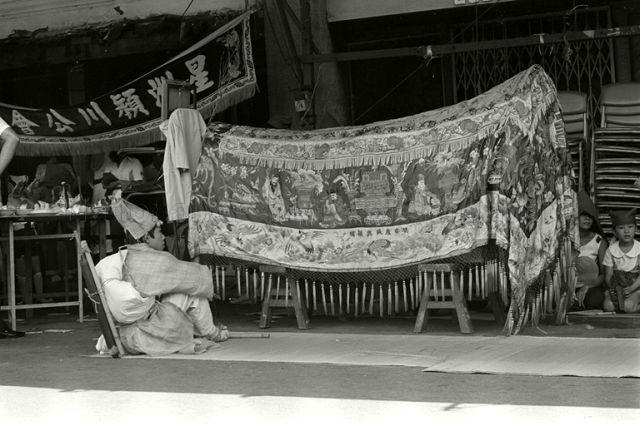 Traditional, Chinese, 'three humped' coffin draped in embroidered covering and mourner at Chinese funeral wake at Clarke Quay