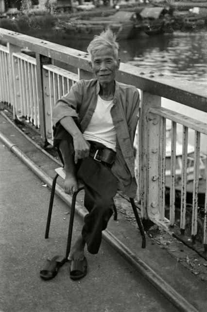 The old story teller at Ord Bridge, with boats on the Singapore River in background
