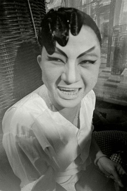 Chinese opera actress with theatrical makeup and hairdo smiling at the camera backstage