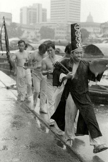 Leng Hiang Tua temple devotees attend to medium Ah Hui, who is  possessed by underworld deity Twa Ya Peh, as he performs rituals along bank of Singapore river on rainy day.