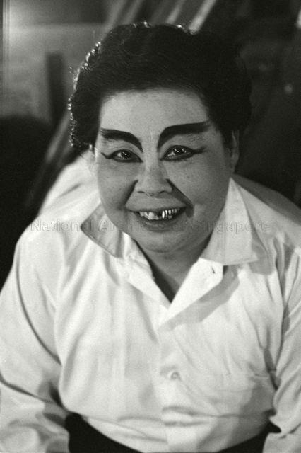 Chinese opera performer with theatrical makeup smiling at the camera backstage