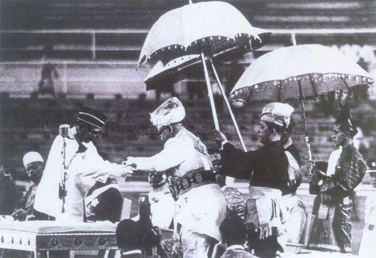 Photo shows the Malaysia Proclamation ceremony held at the Merdeka Stadium, Kuala Lumpur at 8am. The Federation Prime Minister, Tunku Abdul Rahman was seen receiving the "Constitutional Instrument" from the Yang Di-Pertuan Agong, Almarhum Tuanku Syed Putra Al-Haj Ibni Almarhum Syed Hassan Jamalullail from the state of Perlis (standing under the umbrella). All the rulers from the various Malay states were present. The original date for the proclamation was set on 31 August 1963 but was later postponed to 16 September 1963 to allow the United Nations to determine the wishes of the inhabitants of North Borneo and Sarawak in joining Malaysia. The intervention from the United Nations was a result of Indonesia's protest towards the formation of Malaysia.