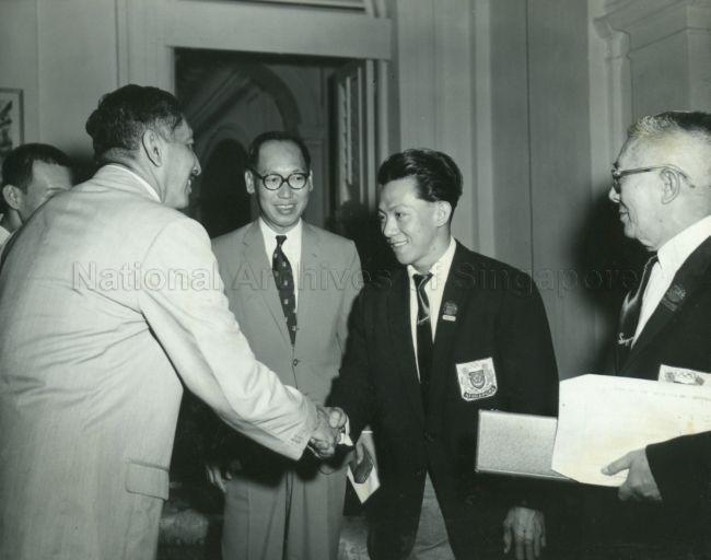 Yang Di-Pertuan Negara Yusof Ishak congratulating Tan Howe Liang, silver medalist for weight-lifting at the 1960 Olympic Games in Rome, during tea party at the Istana Negara