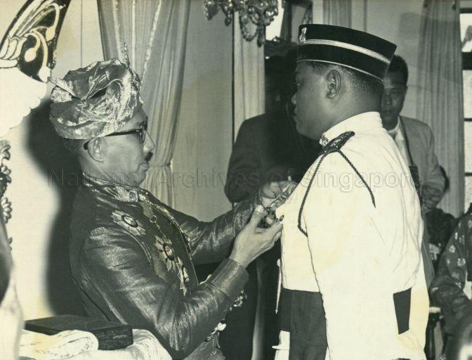 His Highness Sultan Haji Sir Muda Omar Ali Saifuddien of Brunei pinning a medal on his Aide-de-Camp at his birthday celebration