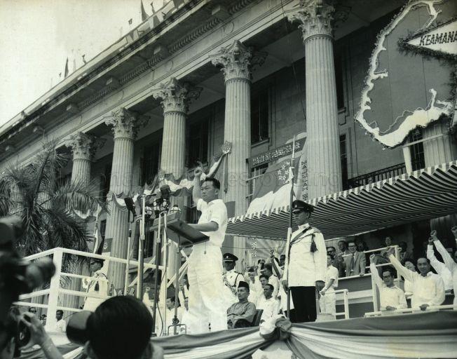 Prime Minister Lee Kuan Yew leading the crowd in shouts of "Merdeka" during a National Day event at City Hall