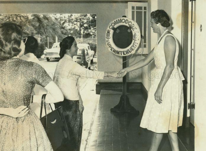 Puan Noor Aishah being greeted by Mrs Blackham, leader of the Red Cross Society's Naval Base group at Sembawang, upon her arrival for a visit