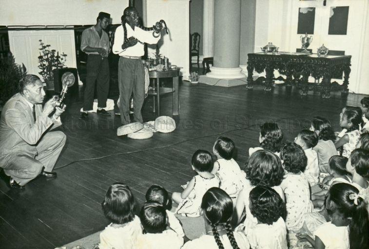 A snake charmer entertaining children of Istana Negara staff at a Christmas party as Yang Di-Pertuan Negara takes photographs