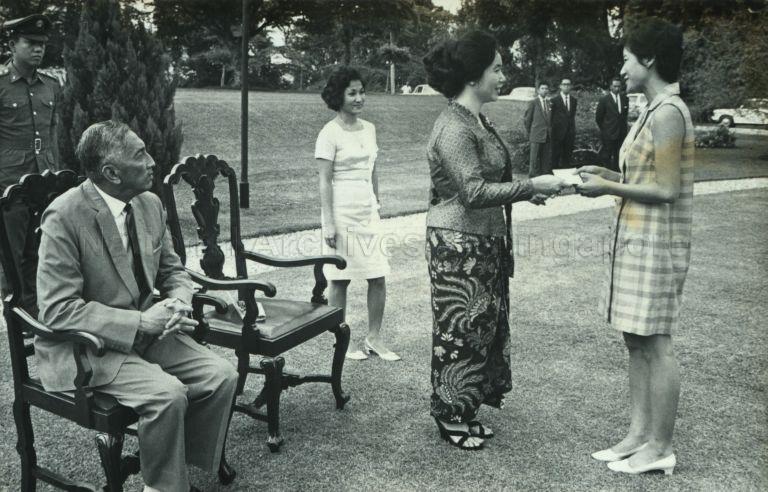 Puan Noor Aishah presenting cheque to representative of a charitable organisation. The cheque is part of money raised from the 17th International Bazaar for the Blind and given out during a reception for helpers of the Bazaar at the Istana. Looking on is President Yusof Ishak, patron of the Bazaar.