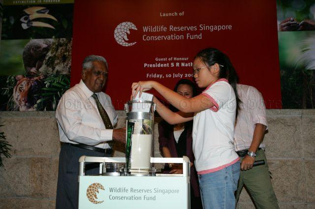 A Chinese girl filling a time capsule with wishes for Singapore's wildlife made by the public, which is scheduled to be opened on 50th anniversary of Singapore Zoo in 2023, during launch of Wildlife Reserves Singapore Conservation Fund (WRSCF), an independent conservation fund dedicated primarily to native wildlife conservation and education, at the zoo in Mandai. Looking on are President S R Nathan and Chairperson of Wildlife Reserves Singapore and WRSCF Ms Claire Chiang (partially hidden).