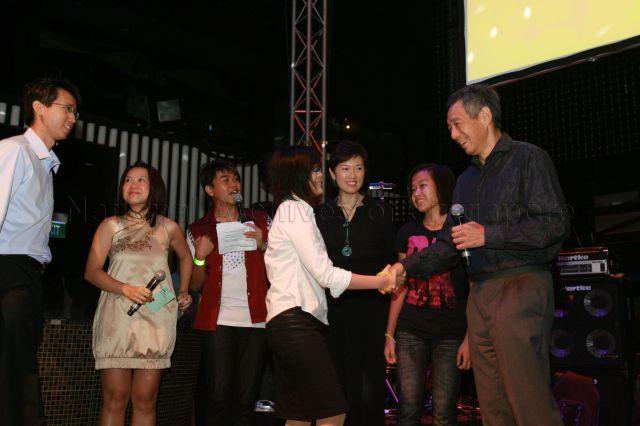Prime Minister Lee Hsien Loong shaking hands with polytechnic student Mandaraz Lim Shi Hui, one of his three assistants for a quiz on Chinese language and modern China, during launch of CLing, a new Chinese-learning media platform (cling.omy.sg) jointly presented by Business China and omy.sg (Singapore Press Holdings' bilingual news portal), at Dragonfly, St James Power Station in Sentosa Gateway. Also present on stage is Member of Parliament for Bishan-Toa Payoh Group Representation Constituency (GRC) and Chief Executive Officer of Business China Mrs Josephine Teo.