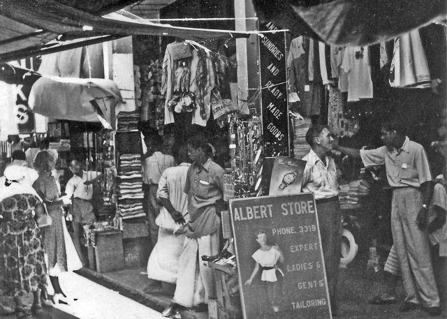 Shoppers in Change Alley, a narrow, congested lane full of shops and stalls offering everything from clothes, batik cloth, bags, brief cases, watches, toys, fishing accessories to handicrafts and other souvenirs. Popular with bargain-hunting servicemen and tourists, c.1950s