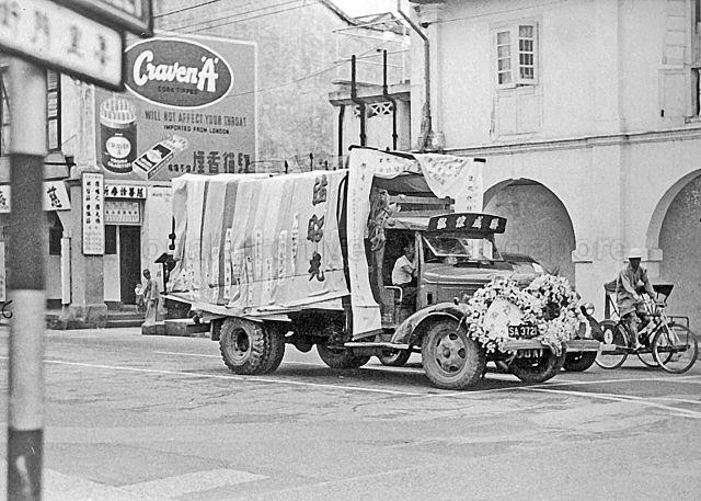 Lorry in a Chinese funeral procession displaying strips of cloth given to family of deceased. Names of the donors are displayed on cloth, c.1950s
