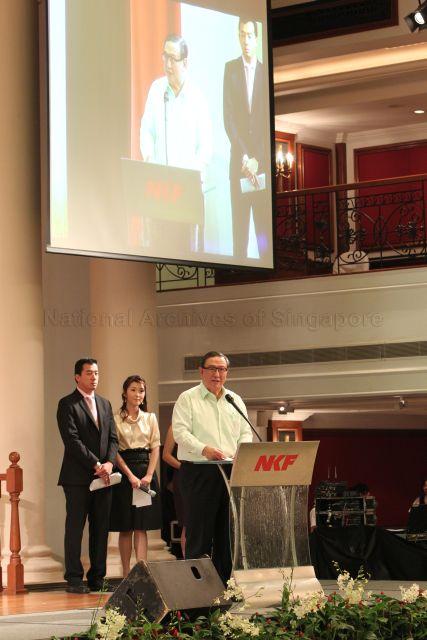 Chairman of National Kidney Foundation (NKF) Gerard Ee speaking at NKF's 100-table charity dinner held at Grand Ballroom, Orchid Country Club. Behind him are Channel NewsAsia presenters Nicholas Fang and Ms Suzanne Jung, the masters of ceremonies for the event.