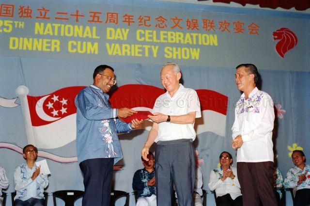 25th National Day Celebration Dinner cum Variety Show at Tanjong Pagar Community Centre - Prime Minister Lee Kuan Yew presenting certificate to Member of Parliament S Chandra Das, with Member of Parliament Ch'ng Jit Koon seated on stage.