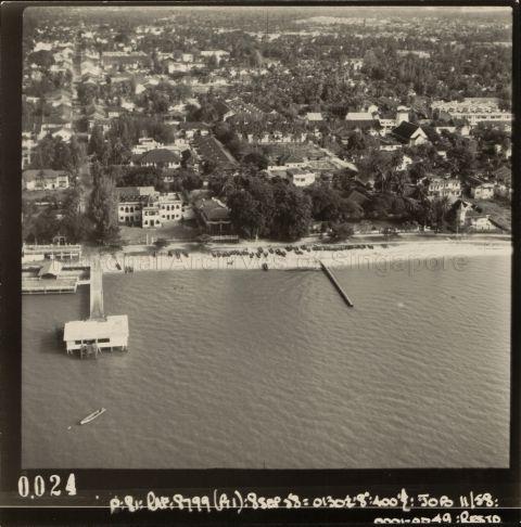 The photograph shows the area around the coastal end of Joo Chiat Road and the former Marine Parade running perpendicular to it along the coast. The former Joo Chiat or Marine Parade Jetty is also visible in the photograph and the former Tung Ling English School, which later became Tung Ling Bible School, on the right hand side of the jetty.