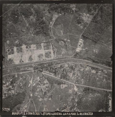 Aerial photo oriented with North on the right, shows the Yew Tee and Mandai Village area. The main road running across the lower third of the photo, on which some lorries are visible, is Woodlands Road. Above Woodlands Road, in the middle-left of the photo, is an area of circular features, which are the remains oil storage tanks. The road running around the bottom and left perimeter of the oil tank farm is Stagmont Ring Road. The track above the oil tanks is Lorong Kedaung. The linear feature below Stagmont Ring Road is the KTM / Malayan Railway line. Below the railway and the row of houses, running beside Woodlands Road in the left third of the photo, and parallel to the railway thereafter, is the Sungei Pang Sua, crossed by some foot bridges from the houses along it. The road that branches off downwards from Stagmont Ring Road near the middle of the oil tank farm and crosses the KTM line, the Pang Sua river, and the Woodlands Road, and splits into three near the bottom of the photo, is Jalan Gali Batu, which led to the granite quarry at Bukit Mandai II. Branching off downwards from Woodlands Road, to the left of Jalan Gali Batu and a small row of houses, is Lorong Kuini. Branching off downwards from 12th milestone Woodlands Road, which is to the right of Jalan Gali Batu and the crescent-shaped side road, is Jalan Kwok Min. In a 1945 map, the area west of the oil tanks (above them in this photo) is called Yew Tee village, and the area east of the Woodlands Road, around Jalan Gali Batu, is called Mandai Village. In later maps from the 1950's onwards, Mandai Village is renamed Yew Tee Village. Below Woodlands Road, at the right edge of the photo, is part of the Kwong Hou Sua Teochew Cemetery. The rural landscape of the area is characterised by vegetable market gardens and rubber plantations.