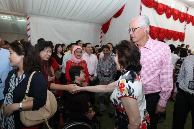 Emeritus Senior Minister Goh Chok Tong's wife Madam Tan Choo Leng (right, side facing camera) is shaking hands with a guest at National Day reception at Istana lawn. Also present are Emeritus Senior Minister Goh Chok Tong (wearing pink attire) and Speaker of Parliament and Jurong Group Representation Constituency Member of Parliament Madam Halimah Yacob (centre).