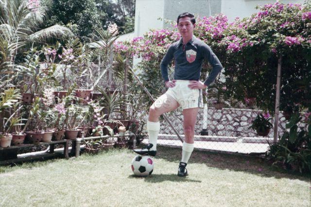 Full-length portrait in colour of Chia Boon Leong at 50 years of age. He is dressed in a China Olympic Football Team jersey posing in his garden with his right leg on a football. He played in the China Olympic Football Team at the 14th World Olympiads in London in 1948.<br />