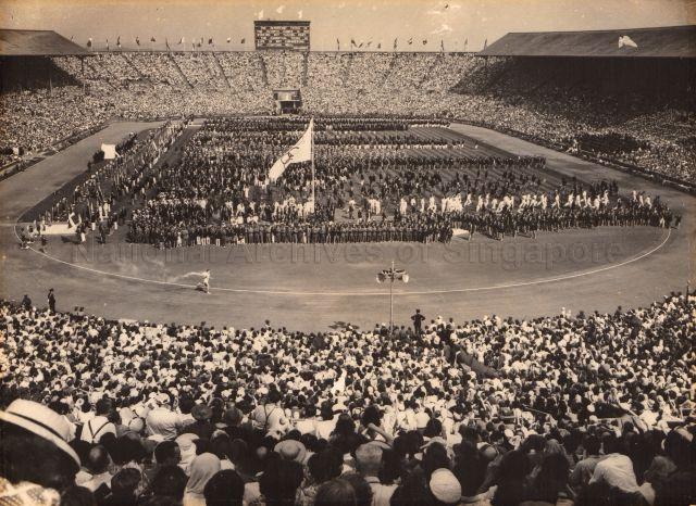 Photograph of the Olympic Flame carrier running on the tracks, seen from the back of a packed London stadium at the 14th World Olympiads in 1948. Chia Boon Leong participated in the China Olympic Football Team.<br />