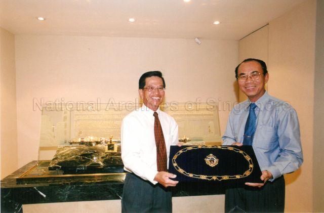 Chairman of Public Utilities Board (PUB) Tan Gee Paw (right) handing over the Mayoral Chain of Office to Chief Executive Officer (CEO) of National Heritage Board (NHB) Lim Siam Kim. The 18-carat gold chain with a pendant medallion bearing the Coat of Arms of Singapore was a gift from Singapore Chinese Chamber of Commerce to the City Council in 1958.<br />