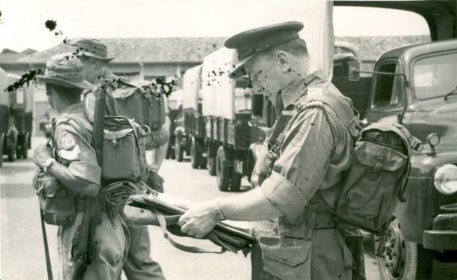 Side view of two soldiers and a Caucasian officer with army vehicles parked in a row beside them during an exercise at Pulau Belakang Mati (Sentosa)
