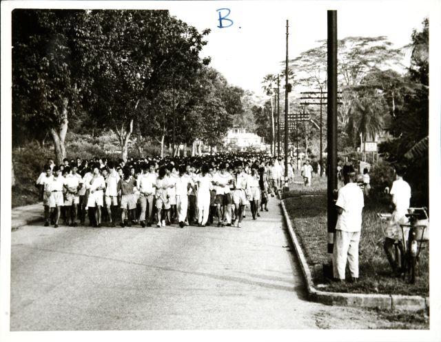 This photograph illustrates one of the incidents in the Report on Military Action taken in the Singapore Riots, 25 October to 2 November 1956. Students marching along a road with arms linked.