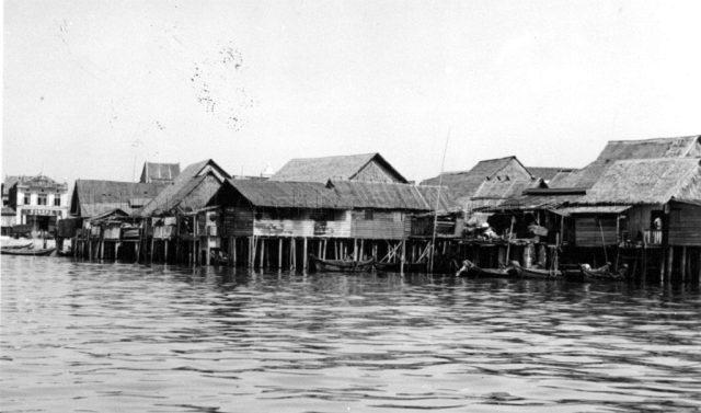 Photograph of a fishing village with attap houses on stilts.