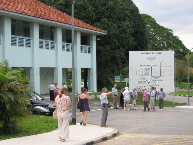 Photograph of Royal Air Force Seletar Association (RAFSA) members standing in front of the Singapore Armed Forces (SAF) Seletar East Camp layout signboard.