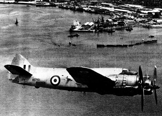 Photograph of Bristol Beaufighter, Britain's famed "Whispering Death" wartime night interceptor fighter aircraft. Aircraft, RD761 is making the Last Operational Sortie from Royal Air Force (RAF) Seletar. The promontory below is Tanjong Pagar with East Wharf. Main Wharf, Albert Dock, Victoria Dock and Empire dock are along the coast behind it.