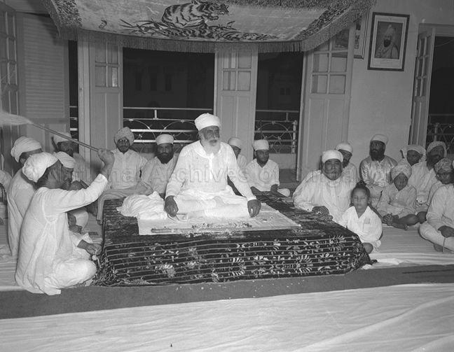 Special prayers held at Bajaj Textiles Raffles Place. Seated right at the back in glasses by the door is Inder Singh Bajaj, owner of Bajaj Textiles. At the far right, the gentleman with his head tilted back wearing a patterned designed turban is Hira Singh Bajaj, younger brother of Inder Singh Bajaj. Hira Singh Bajaj is joint owner of Gian Singh &amp; Co next door to Bajaj Textiles at 30 Raffles Place.