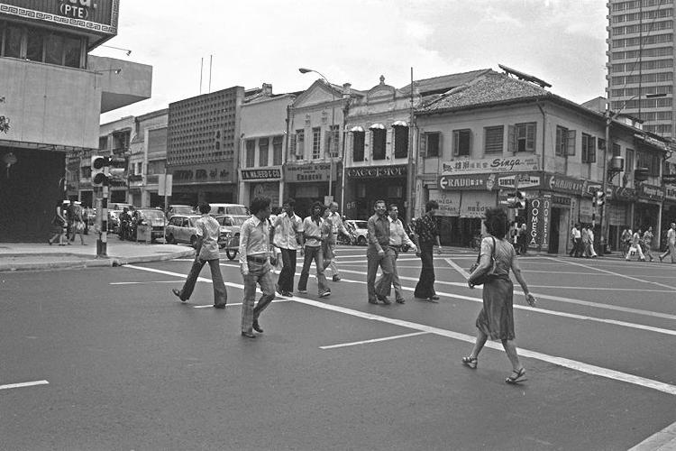 View at the junction of North Bridge Road and Coleman Street.  On the left is the Chinese Emporium while Peninsula Hotel is the tall building on the right.  Well known stores such as Metro, S A Majeed and Excelsior Pte Ltd, can be seen at Coleman  Street.